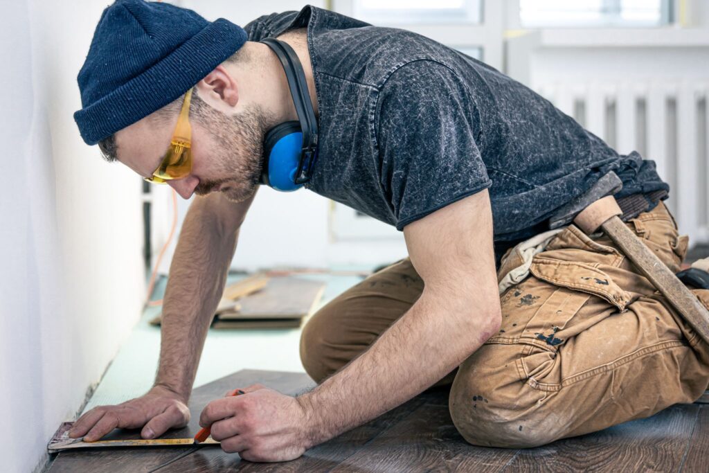 A man wearing headphones is working on a wooden floor.